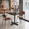 Cafétisch Prisma 70x70 cm mit schwarzer Marmoroptik und Kreuzgestell in einem modernen Café-Ambiente.